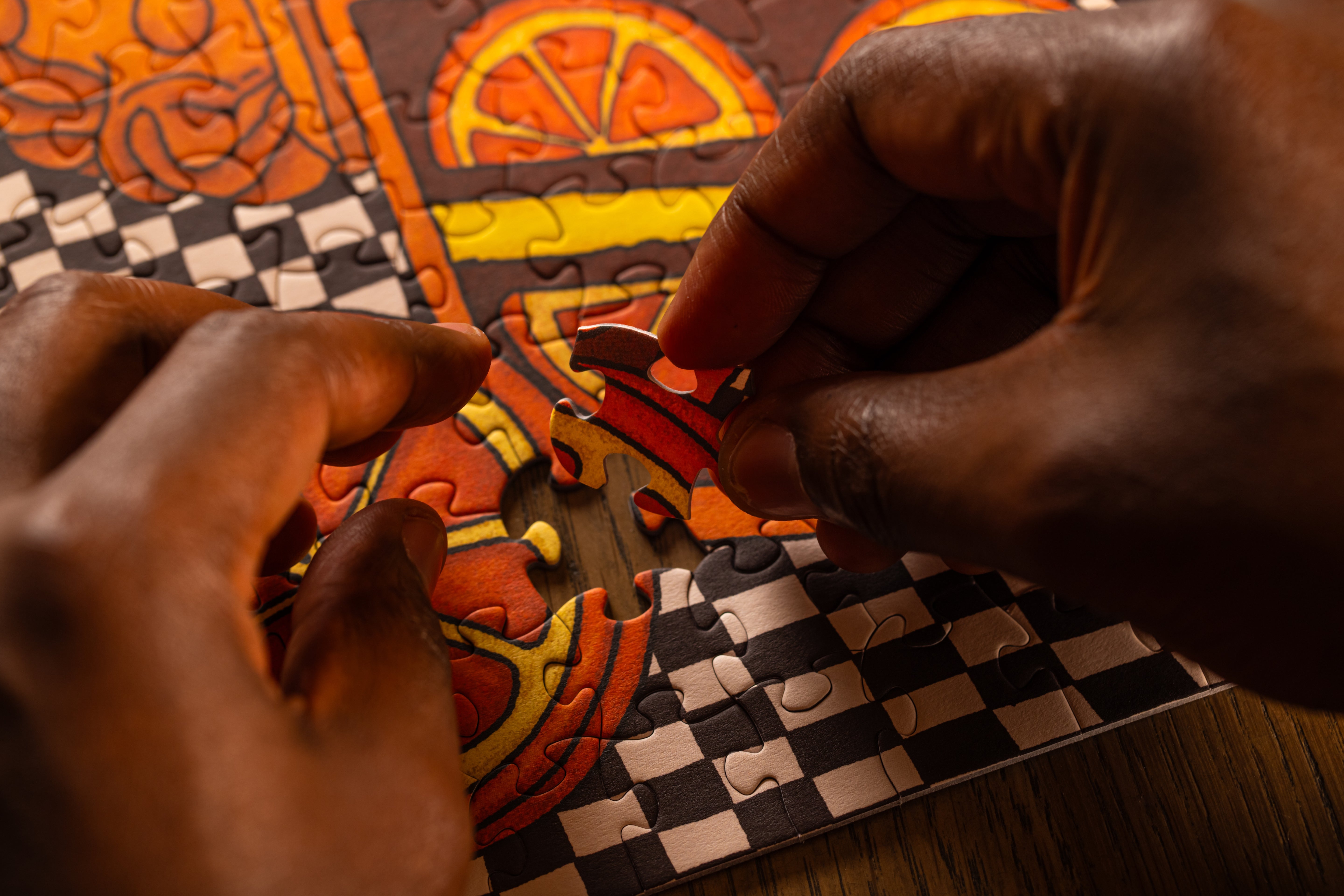 A person carefully inserting a puzzle piece into the orange citrus cake section of the Huntley House Frosted Feelings jigsaw puzzle