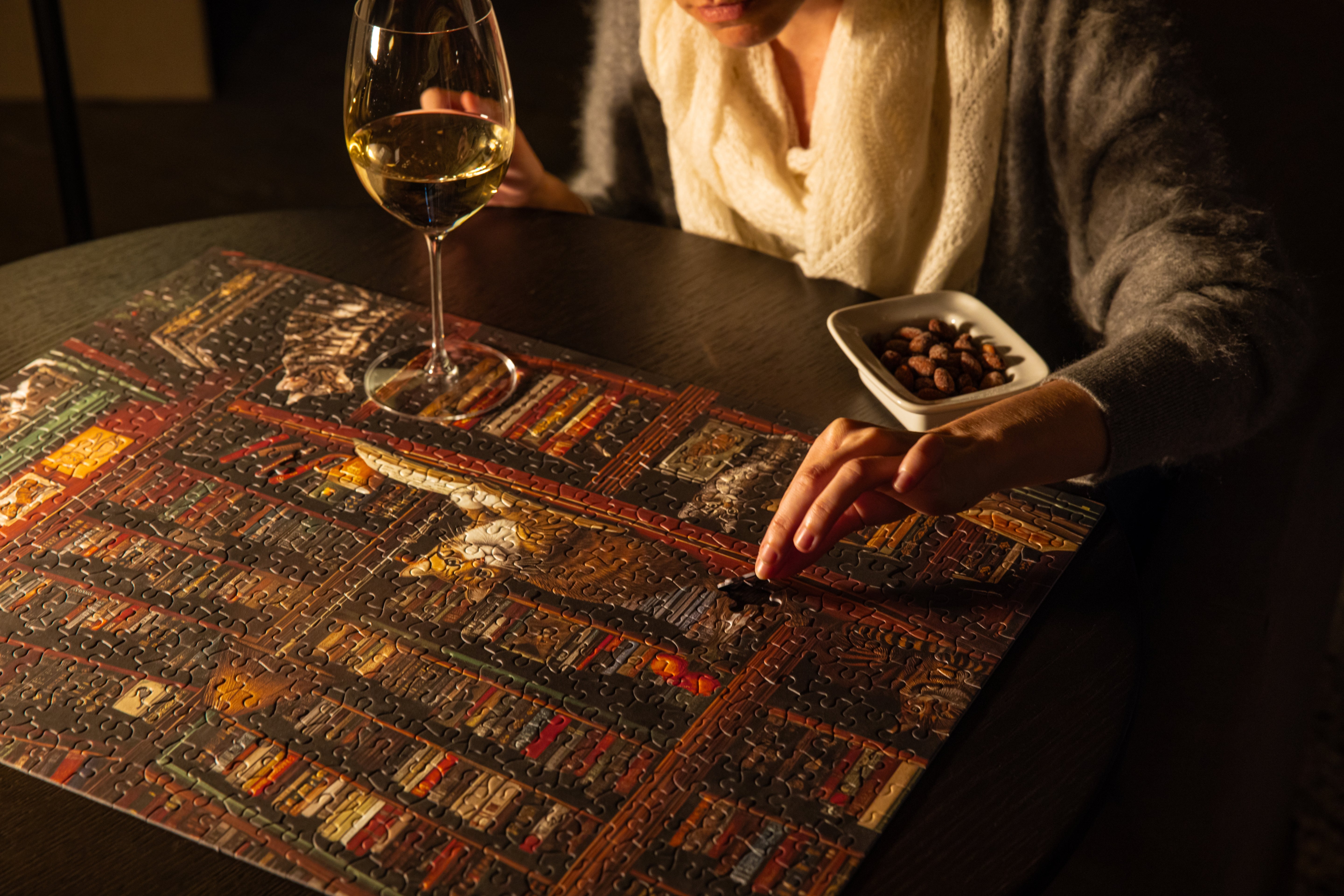 A woman assembling the Huntley House Purrfect Pages jigsaw puzzle on a wooden table