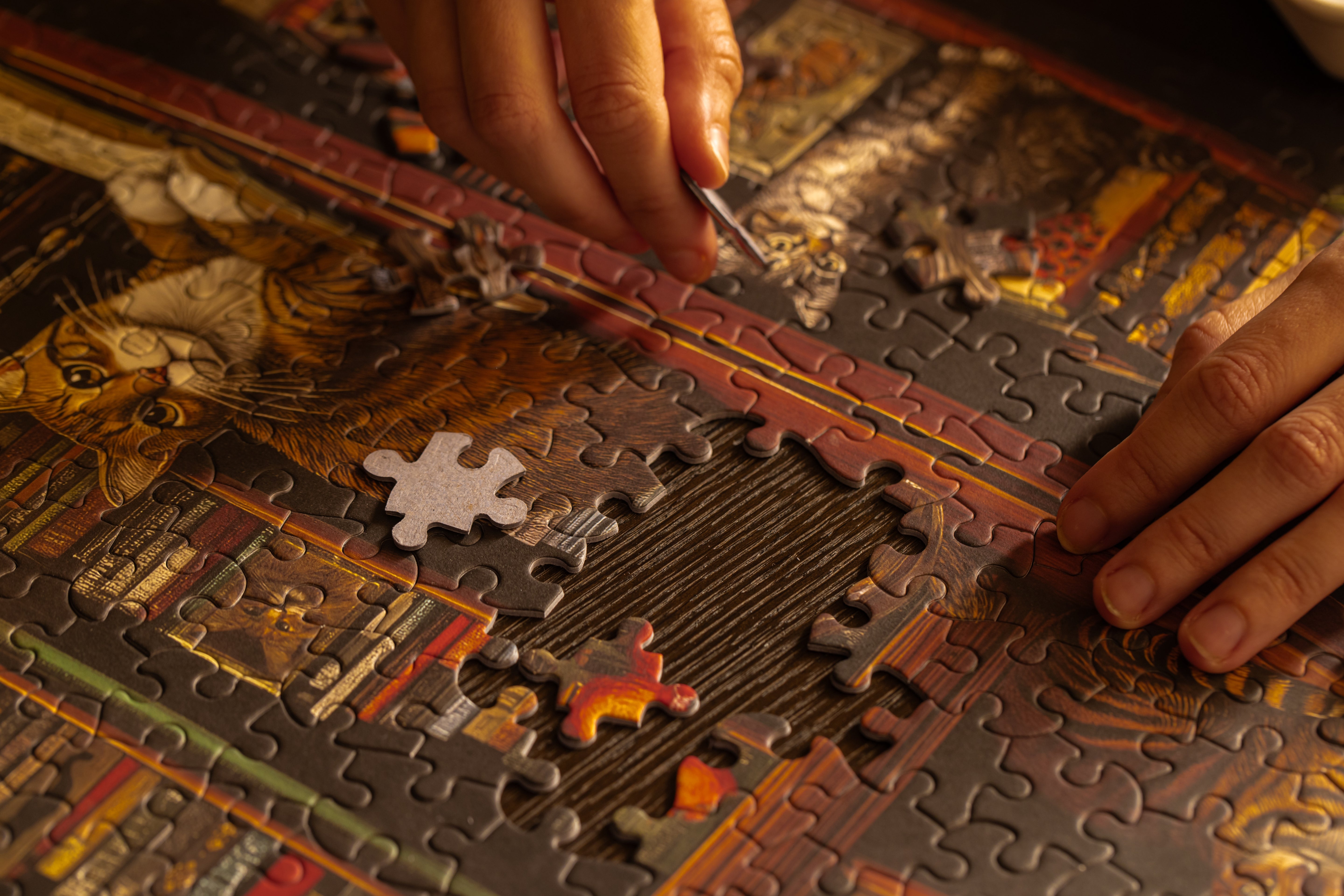 A woman assembling the Huntley House Purrfect Pages jigsaw puzzle on a wooden table