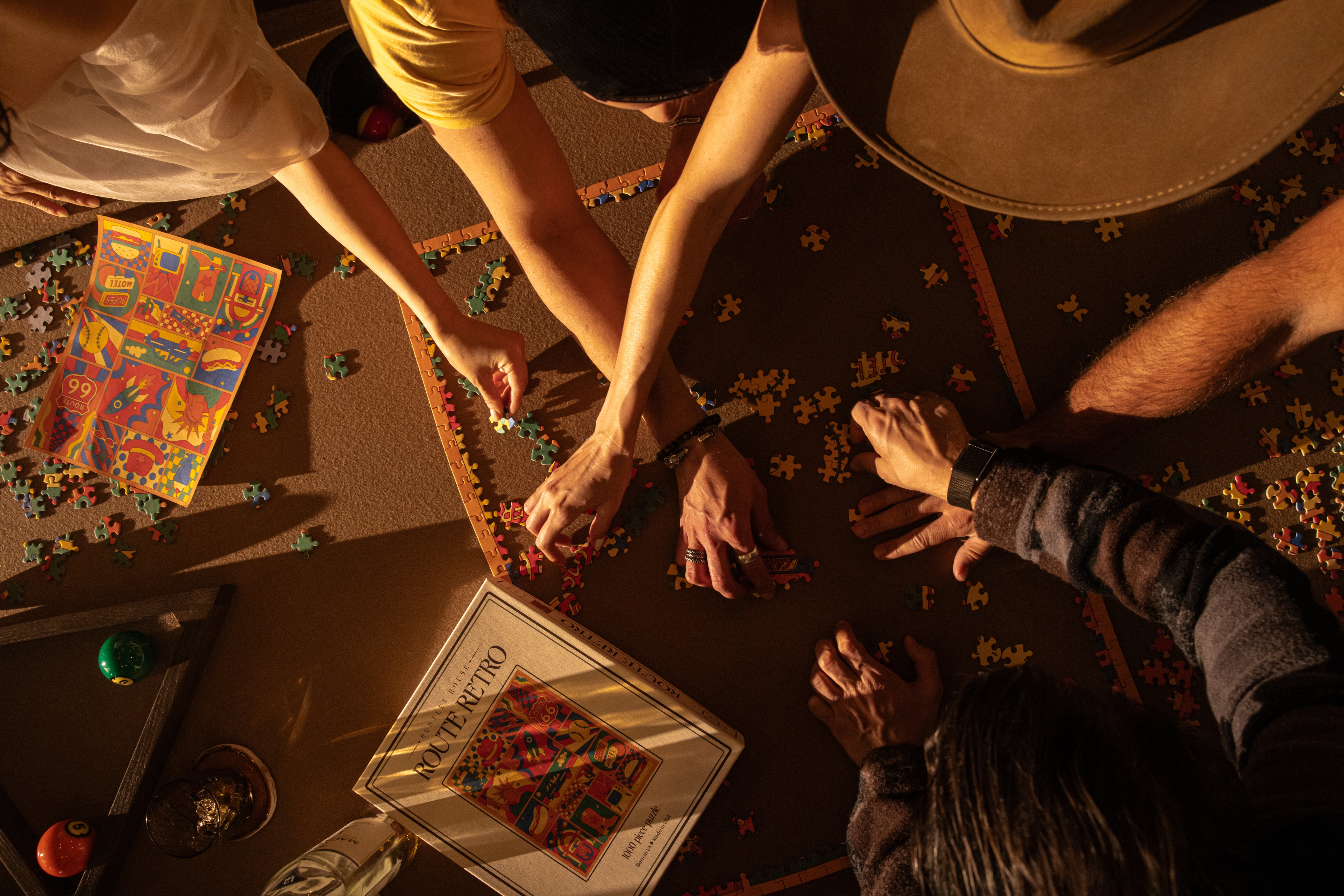 Top-down lifestyle view of a group of people assembling the Huntley House Route Retro 1000 piece puzzle together on a table