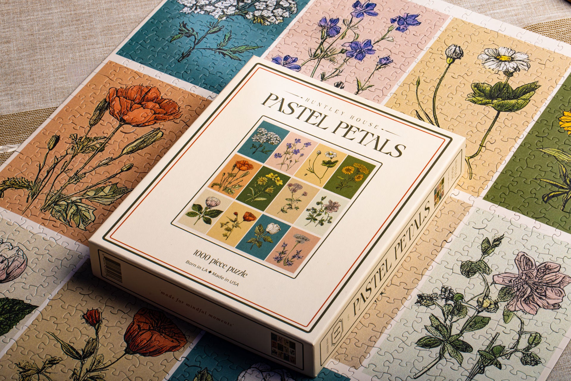 A lifestyle view of the Huntley House Pastel Petals puzzle box sitting on top of the completed vintage floral jigsaw puzzle